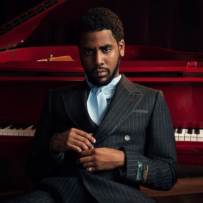 Jharrel is posing in a suit with piano in the background.